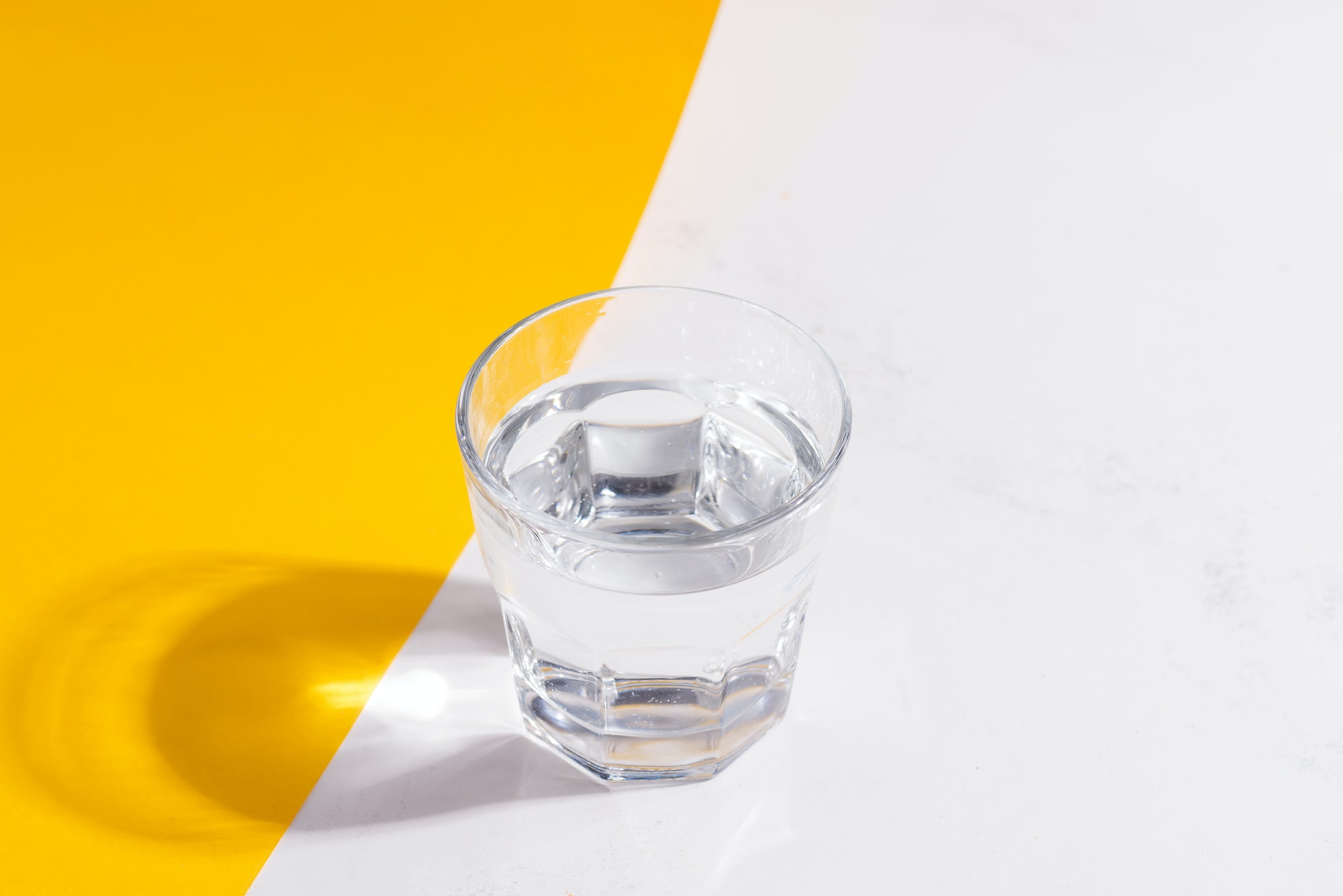 Top view of glass of fresh cold clean water on a duotone yellow white background with soft shadows