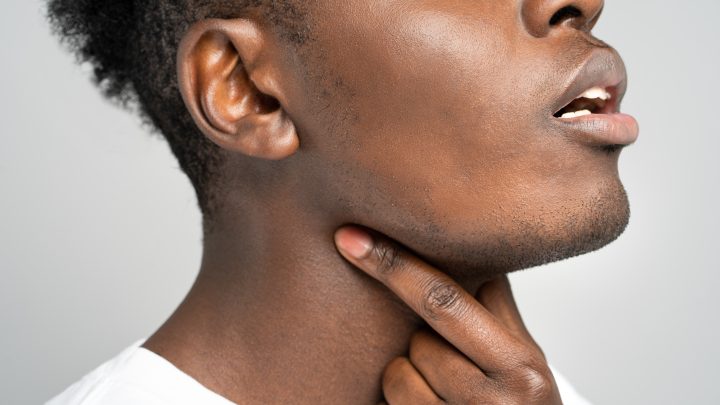 Black man touches fingers of sore throat, thyroid gland, isolated on studio gray background